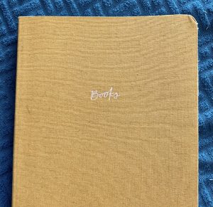 A yellow notebook on a blue textured background. The notebook says Books on the cover.